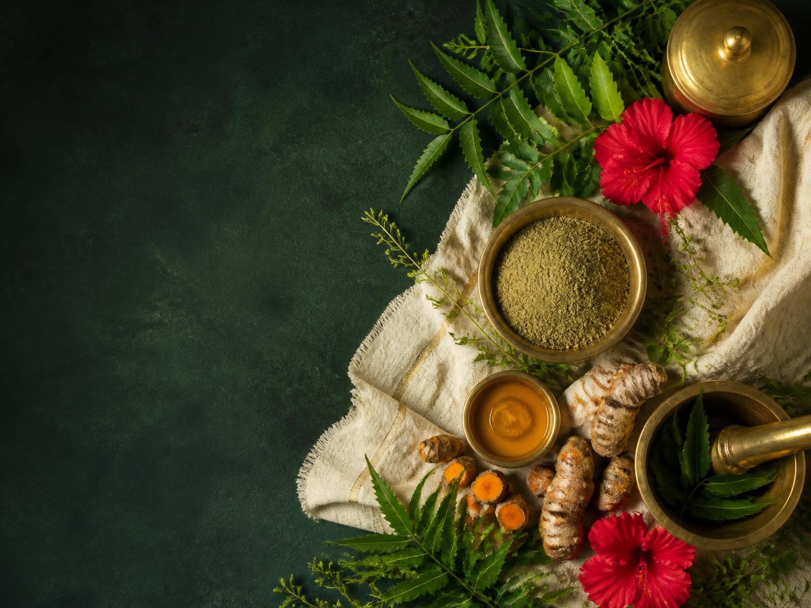 Herbs, hibiscus flowers, turmeric and brass bowls of herbal powder on cream linen